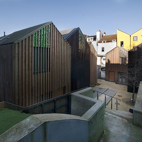 Rear detail view showing cladded buildings and concrete slope and steps with metal handrail leading to the development