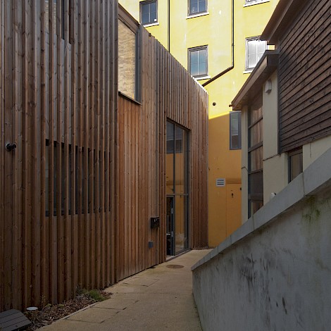 Angled shot looking down past wood clad units towards bright yellow buildings in the sun