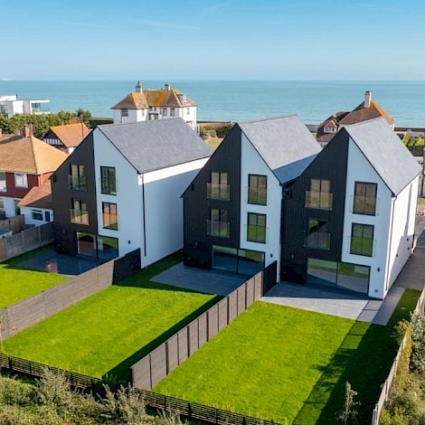 Aerial shot of contemporary house with sea view at the rear on a sunny day with laid to lawn gardens